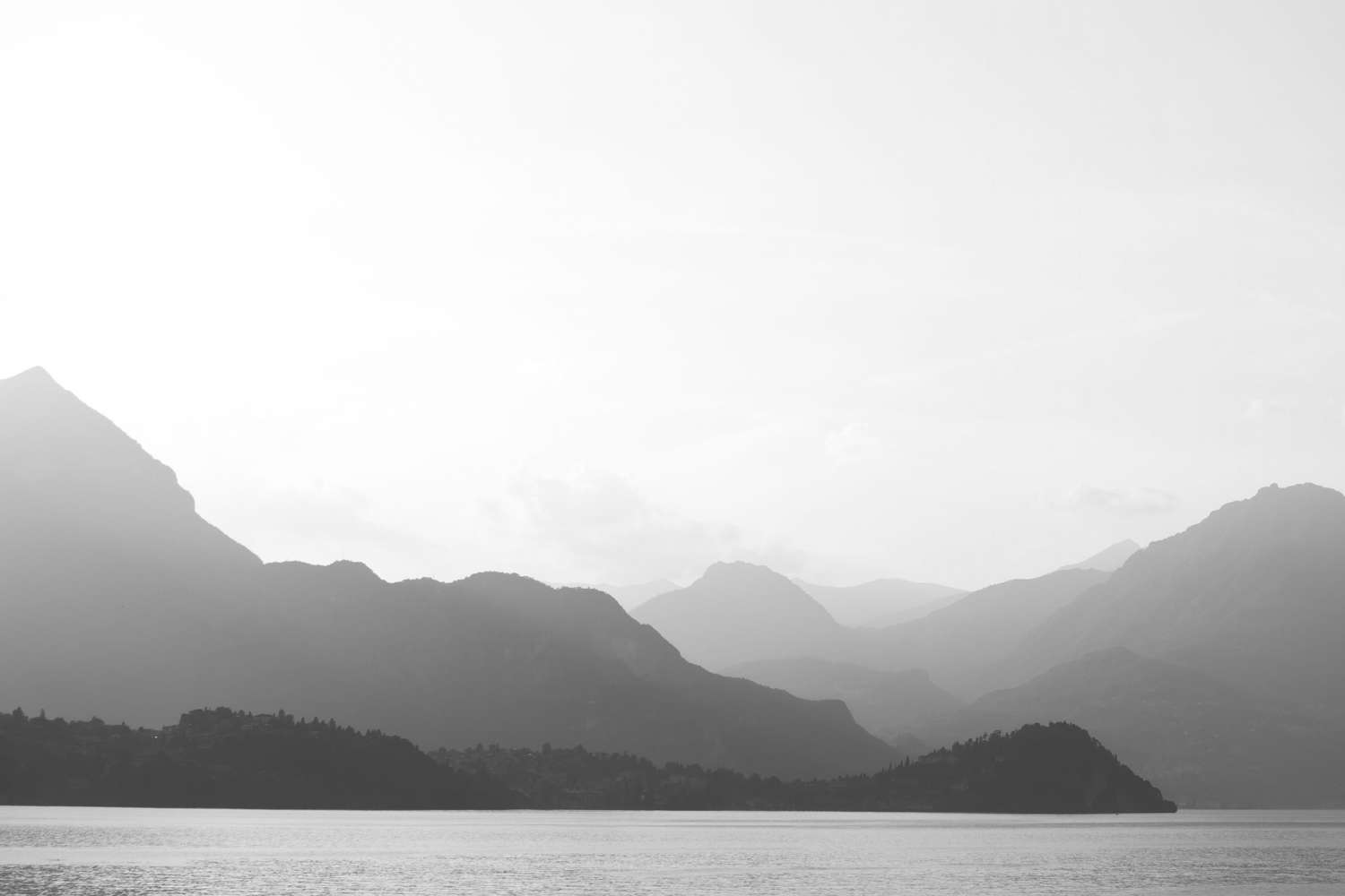 Schwarzweißbild eines ruhigen Sees, umgeben von Bergen. Die Berge liegen geschichtet im Hintergrund und erzeugen eine neblige, ätherische Atmosphäre, die an eine ruhige CBD-Oase erinnert. Ruhiges Wasser im Vordergrund reflektiert das gedämpfte Licht und trägt zur Ruhe der Szene bei.